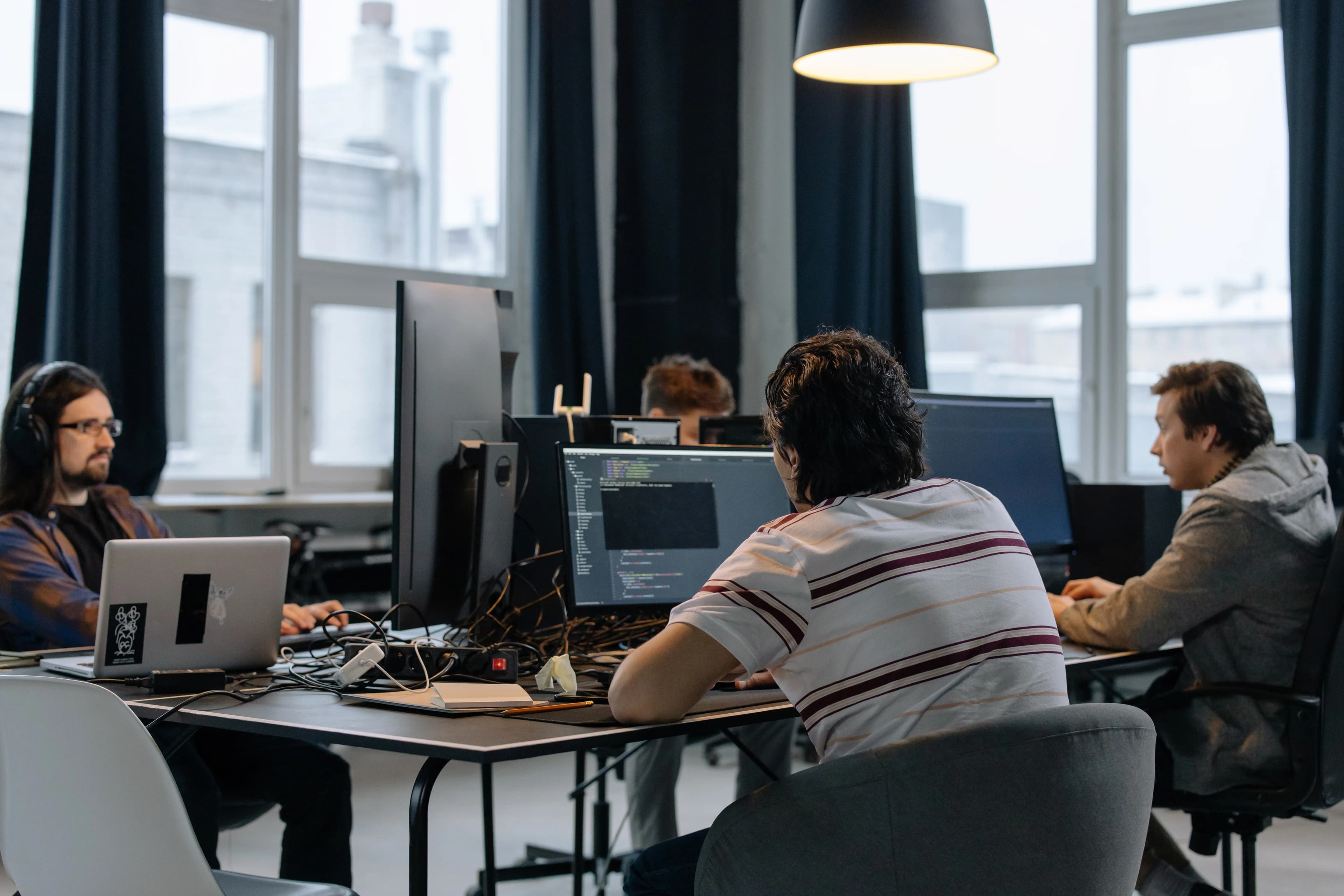 Software developers collaborating at desks with multiple monitors in an office.