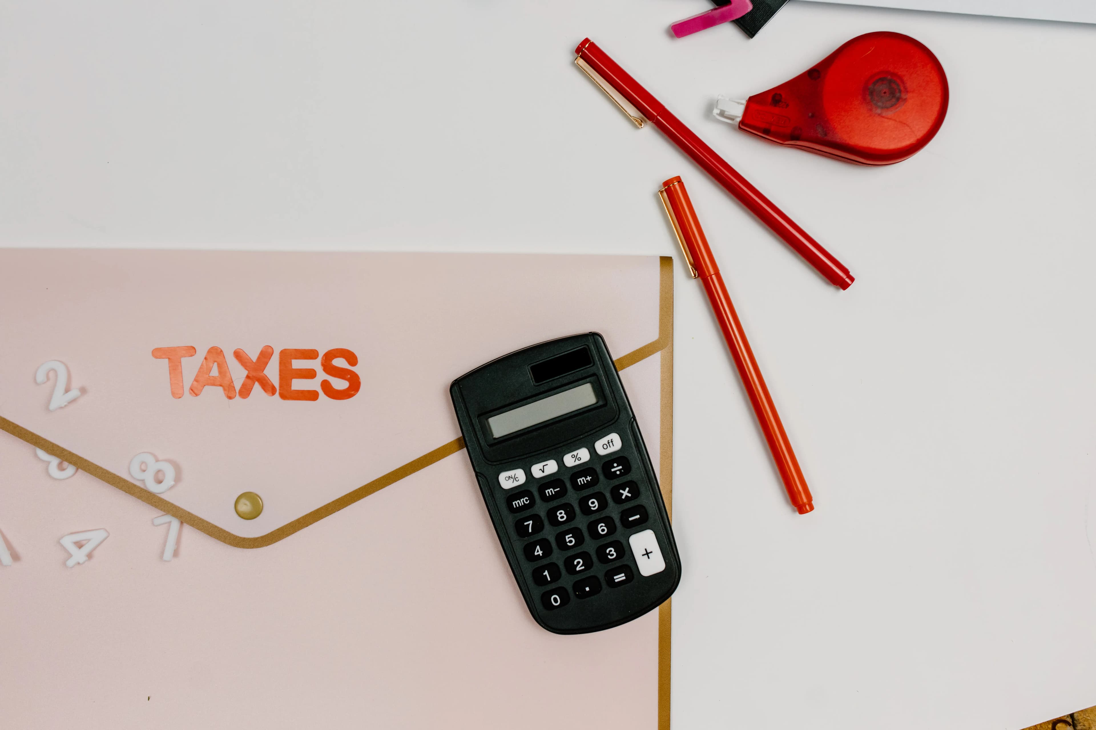A calculator and pens beside a folder labeled taxes.